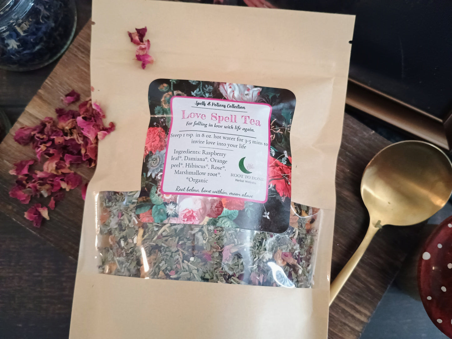 Love spell tea package with a label on a wooden surface with dried flowers and a spoon.