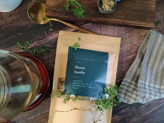 Tea package labeled 'Throat Soothe' on a wooden surface with herbs and a teapot.