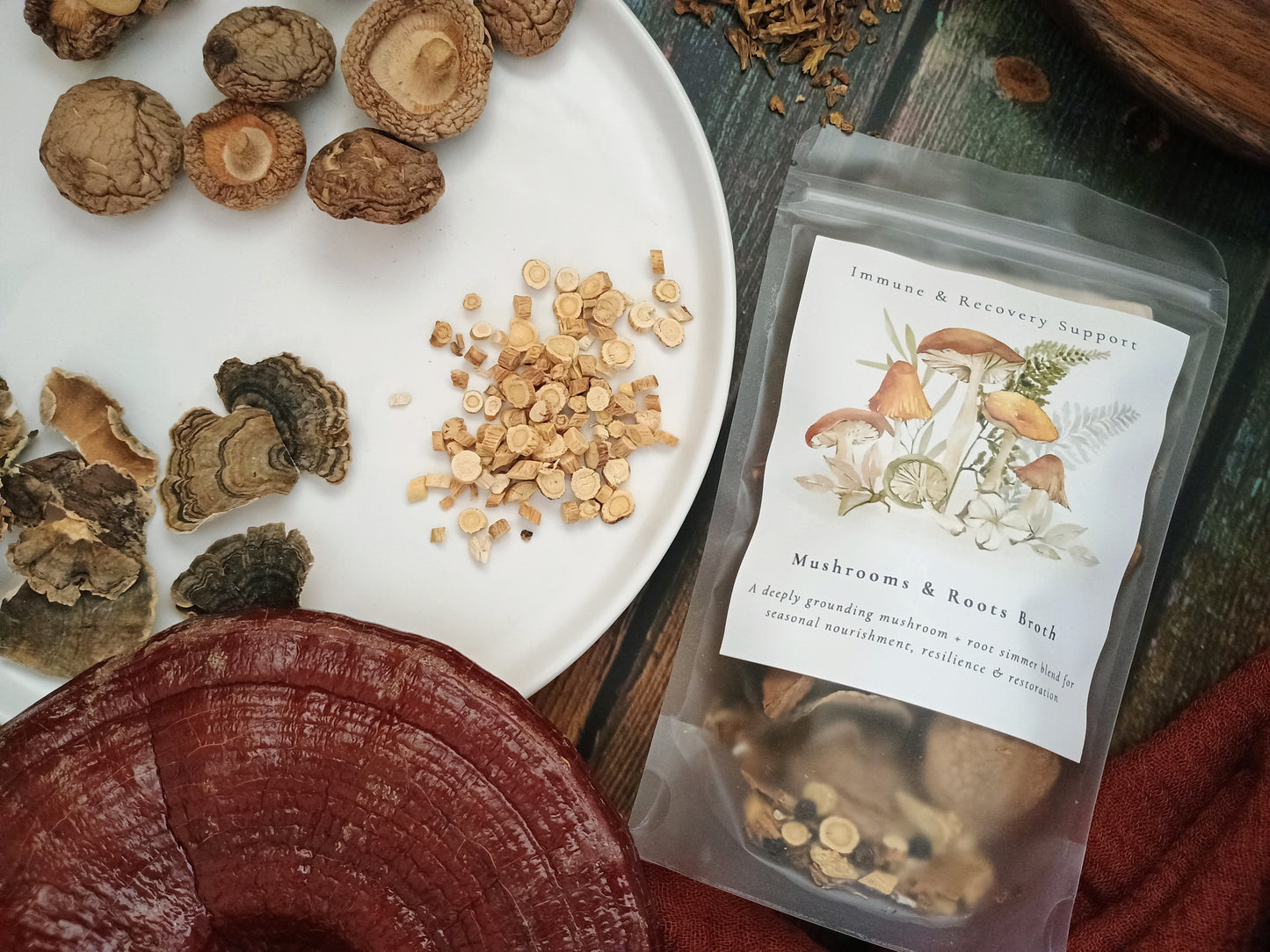 A clear stand-up pouch labeled 'Mushrooms & Roots Root' containing dried mushrooms and roots, styled on a rustic wooden surface with loose mushrooms and sliced mushrooms around it.