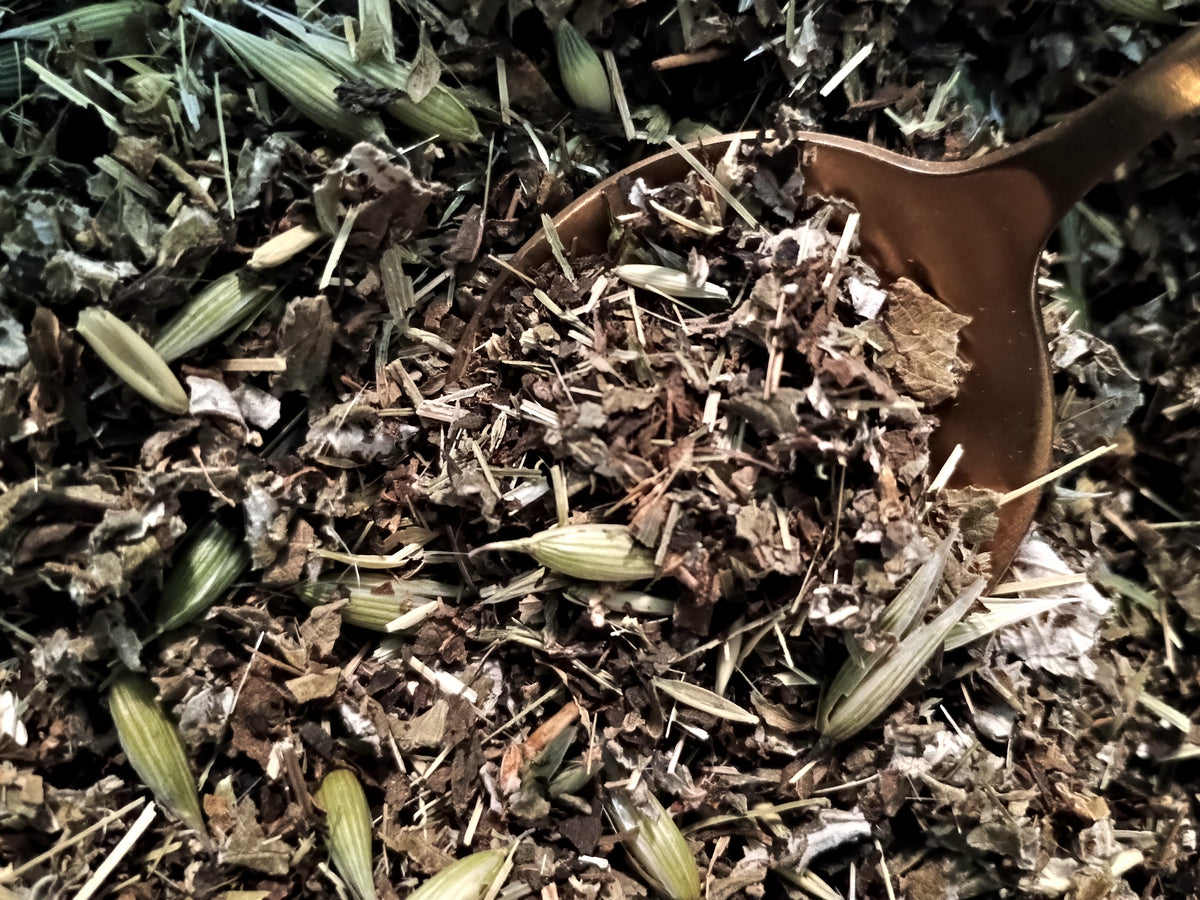 Close-up of loose dried herbs and botanicals with a wooden spoon scoop in a natural outdoor setting.