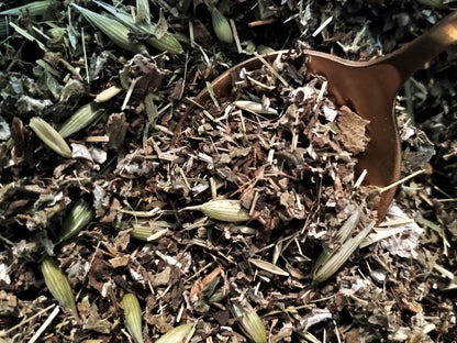 Close-up of loose dried herbs and botanicals with a wooden spoon scoop in a natural outdoor setting.
