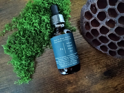 An amber glass dropper bottle labeled 'Root to Bone Herbal' placed on a wooden surface beside green moss and a dark honeycomb-like decorative object.