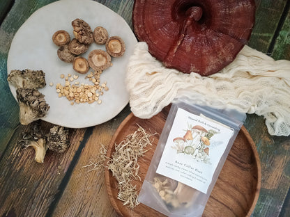 A styled flat-lay of raw mushroom products on a rustic wooden table, featuring a clear pouch of raw celery and mushroom blend, a large red reishi mushroom, sliced shiitake mushrooms, dried morels, and herbal pieces on a white plate and wooden tray.