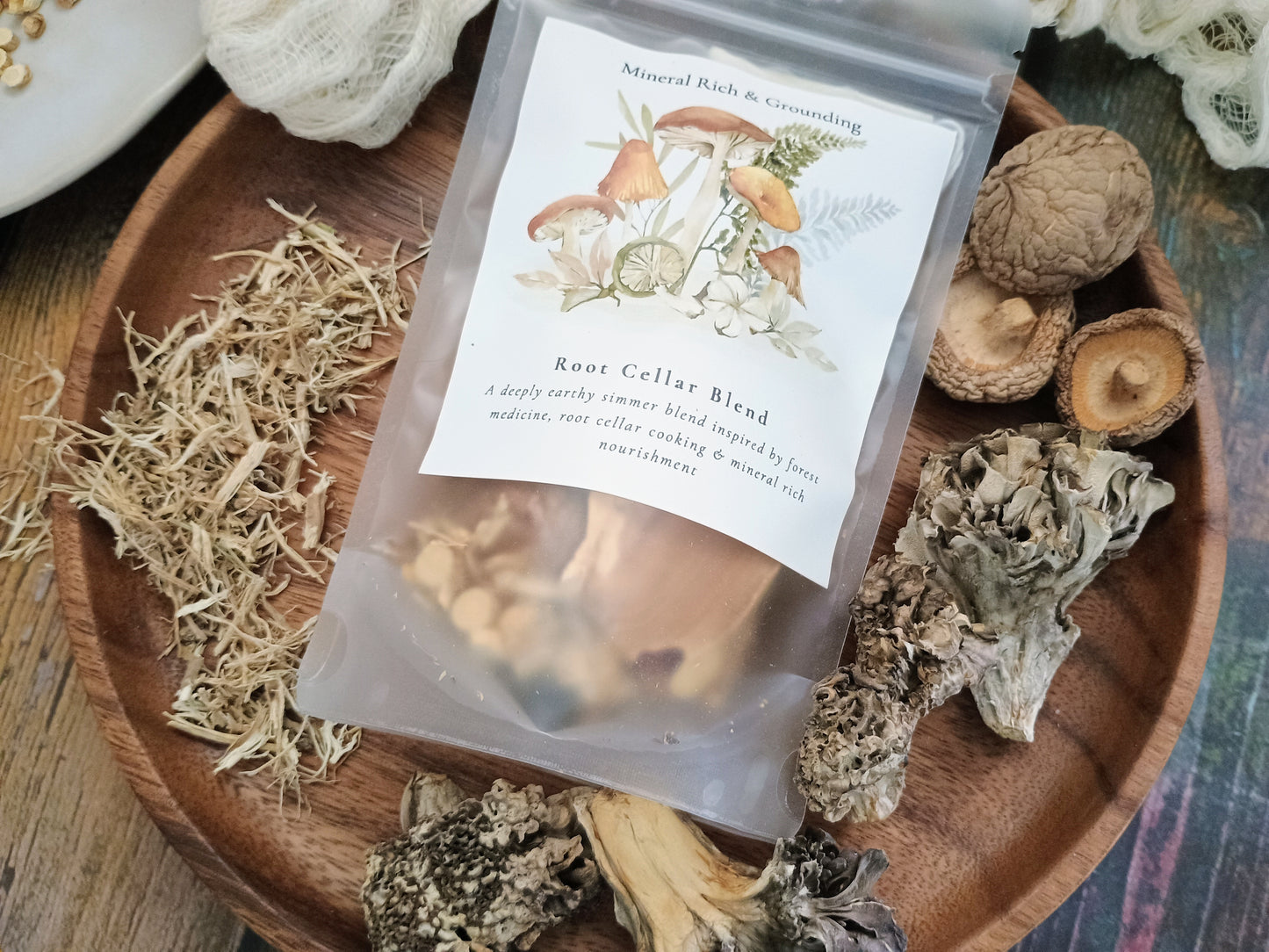 A clear stand-up pouch labeled 'Root Cellar Blend' with mushroom illustrations, placed on a wooden tray surrounded by dried mushrooms and herbs.