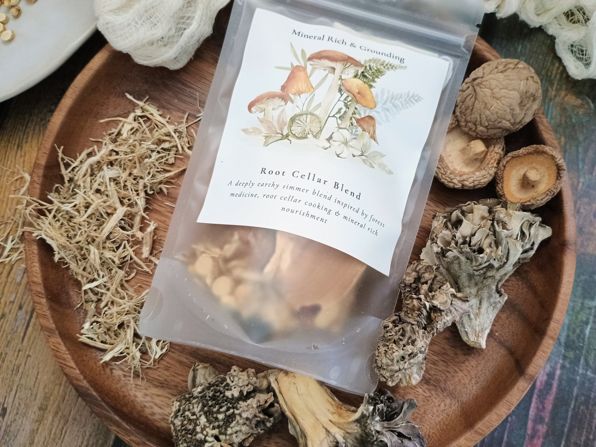 A clear stand-up pouch labeled 'Root Cellar Blend' with mushroom illustrations, placed on a wooden tray surrounded by dried mushrooms and herbs.