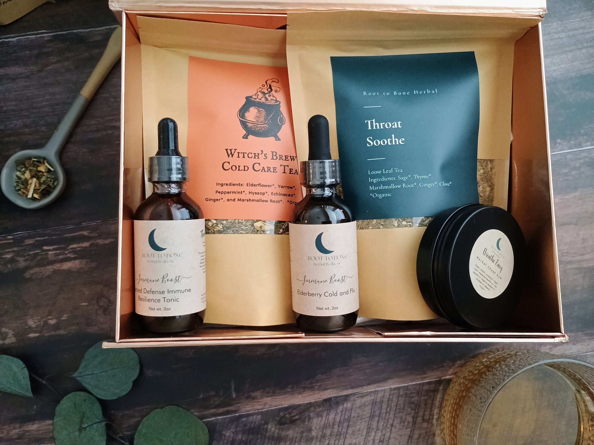 Herbal wellness kit with bottles, tea bags, and a salve in an open box on a wooden surface.