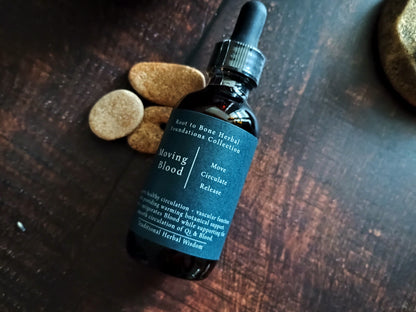 A dark amber glass dropper bottle labeled 'Moving Blood' from Root to bone Herbal Foundations Collection, placed on a dark wooden surface with three small round herbal tablets nearby.