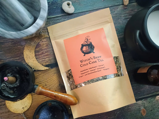 Bag of 'Witch's Brew Cold Care Tea' on a wooden surface with tea-making items.